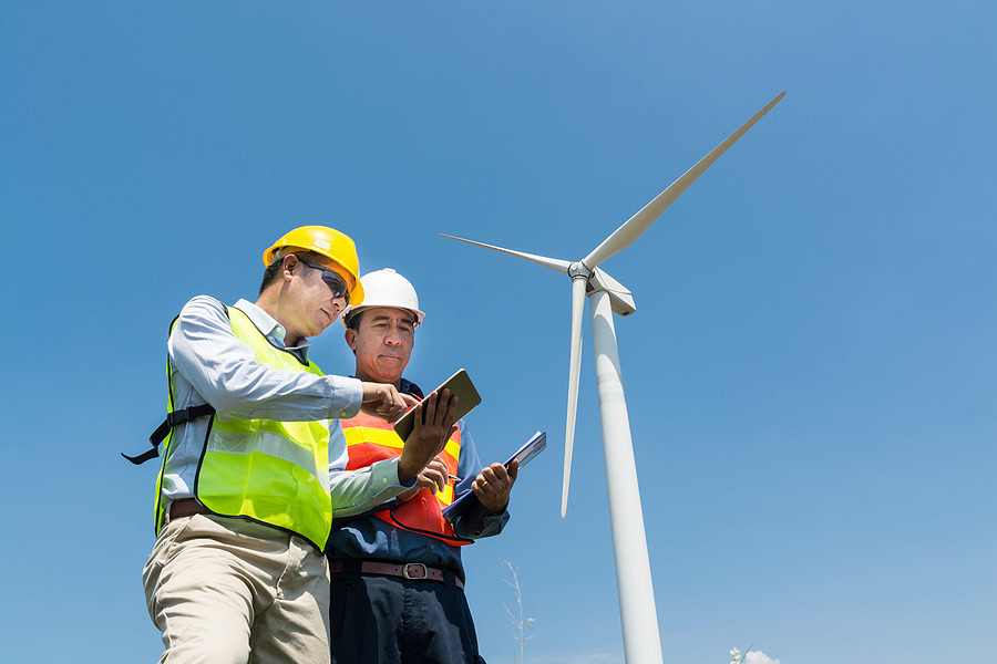 Alternative Power Or Renewable Energy Technology Project Development Concept, Engineer And Architect Discuss Over Digital Wireless Tablet And Clipboard While Working At Wind Turbine Power Generator Tower Site.