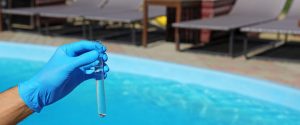 A gloved hand holding a vial of water, in front of a pool