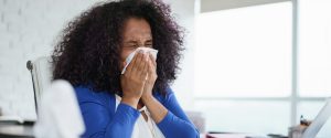 Woman sneezing in office representing the poor air quality in office.