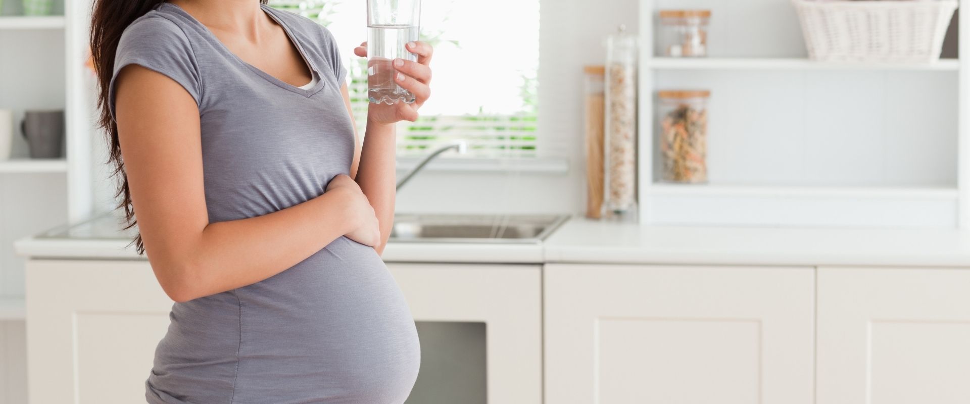 A pregnant woman drinking water in a kitchen