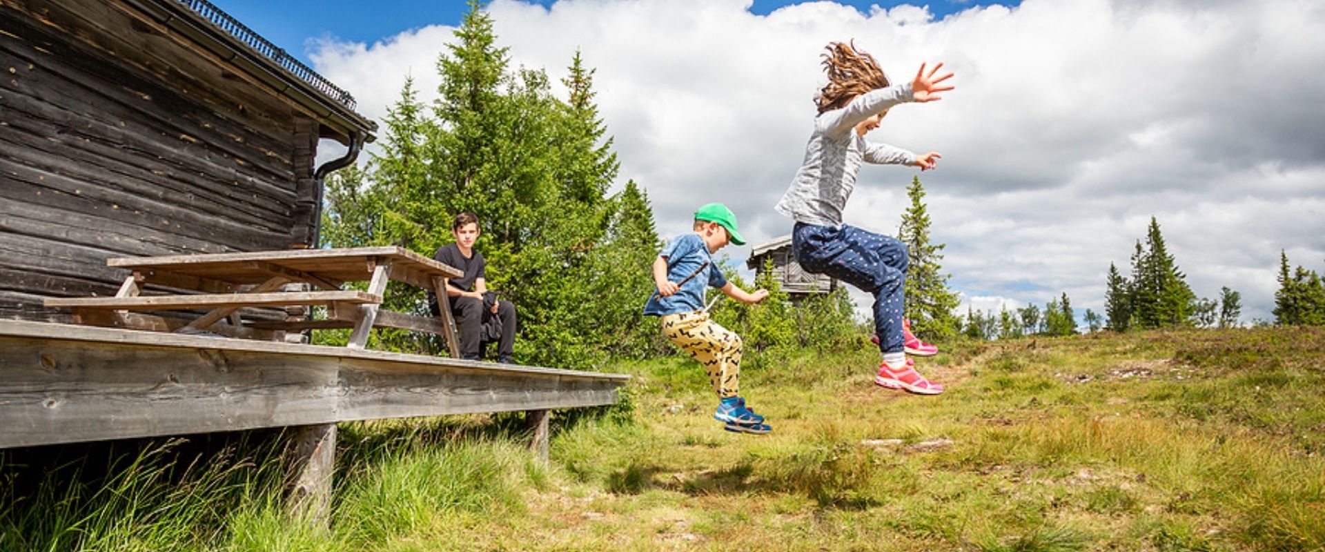 Summer nature side view of children in mid air jumping of a porch landing on grass hill